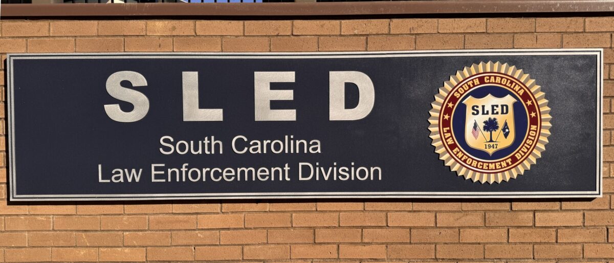 A sign on a brick wall reads "SLED South Carolina Law Enforcement Division" with the SLED shield emblem featuring an eagle and the state seal on the right side.