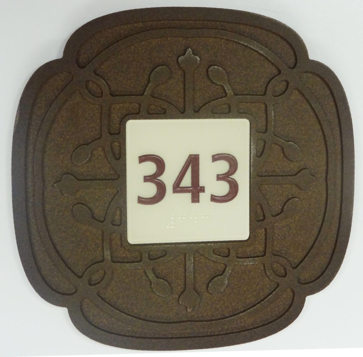 A decorative plaque with an ornate brown border features the number "343" in bold red digits at the center on a white background. The border design includes symmetrical patterns that resemble floral motifs.