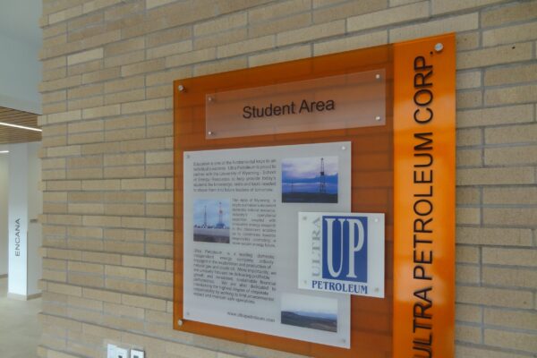 A wall-mounted informational display titled "Student Area" includes text and images, with the "Ultra Petroleum Corp" logo prominently featured alongside. The background is a light brown brick wall.